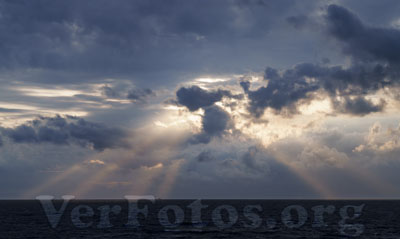 el cielo del atardecer se tiñe de tonos cálidos mientras el sol se oculta lentamente tras las nubes, iluminando el mar con destellos dorados, costa de Donostia-San Sebastian, Euskadi