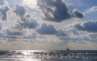 En el atardecer de Donostia-San Sebastián, un barco navega por el mar, mientras nubes adornan la costa bajo el sol.