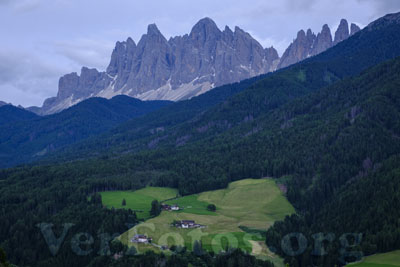 Bajo las montañas, los caseríos emergen entre prados verdes, creando un paisaje idílico donde la naturaleza y la tranquilidad se abrazan, valle dde Funes, Italia.