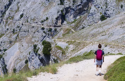 Mujer hace senderismo en la Ruta del Cares, Picos.
Una mujer camina por un sendero de tierra en la Ruta del Cares. El camino recorre el Parque Nacional de los Picos de Europa. La fotografía muestra la práctica del deporte de senderismo en la naturaleza. El paisaje incluye montañas de piedra y un camino largo. Esta imagen es un recurso gratuito y solidario disponible para descargar en formato digital para proyectos visuales.